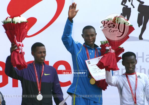 Geoffrey Mutai (R) of Kenya waves after winning gold in the men's  event of Delhi half Marathon, along with silver medallist Lelisa Desisa (L) of Ethiopia and bronze medal winner Yacob Yarso of Ethopia during the victory ceremony , in New Delhi